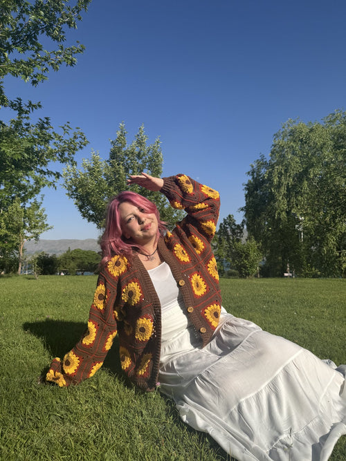 Customer sitting on grass in a brown sunflower crochet cardigan