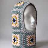Teal and mustard granny square balaclava on a display head, open face and deep neck section — handmade by Ana Chic