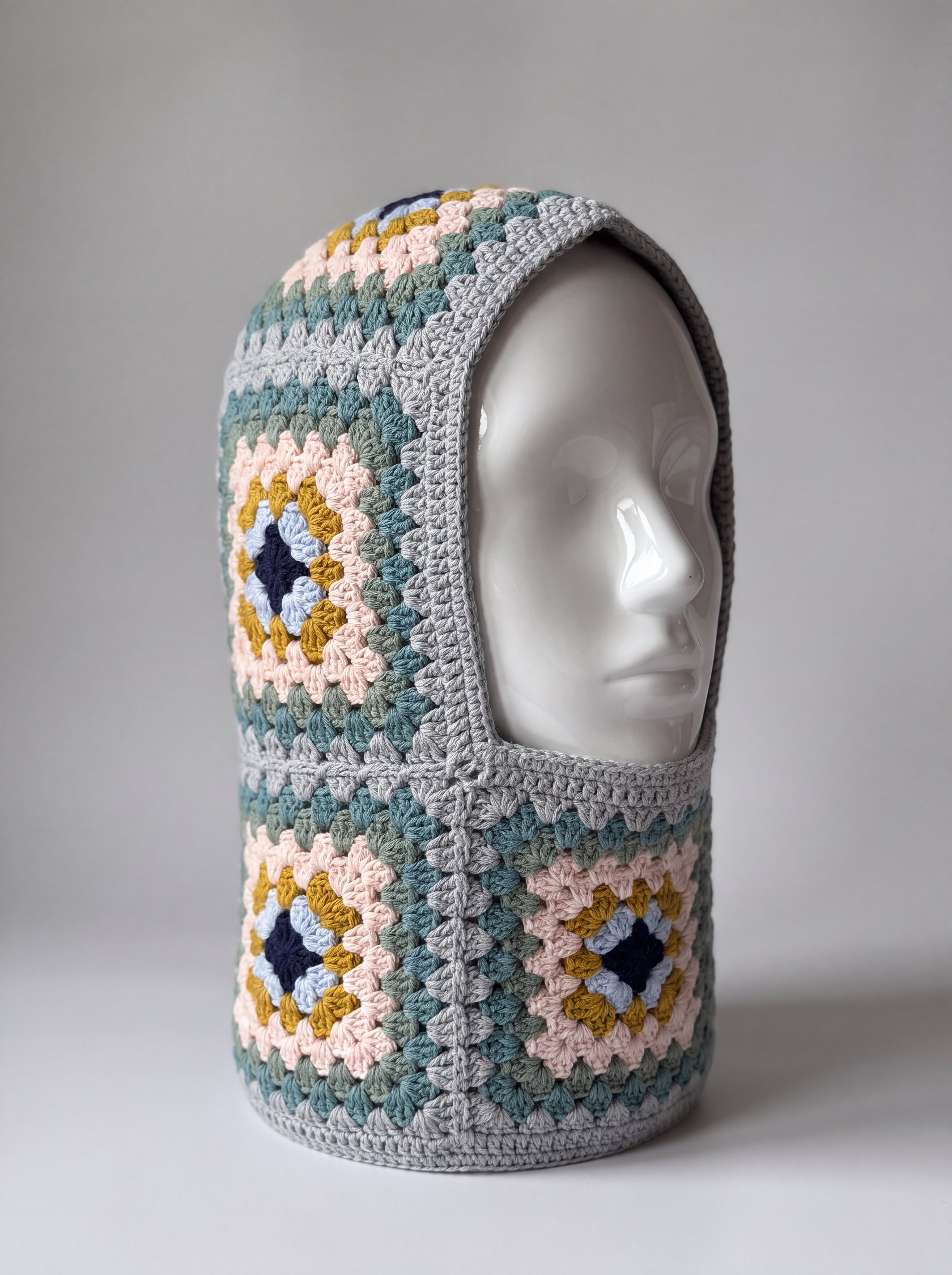 Teal and mustard granny square balaclava on a display head, open face and deep neck section — handmade by Ana Chic
