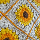 Close-up of a crocheted sunflower square with yellow puff-stitch petals on the cream shoulder bag — handmade by Ana Chic