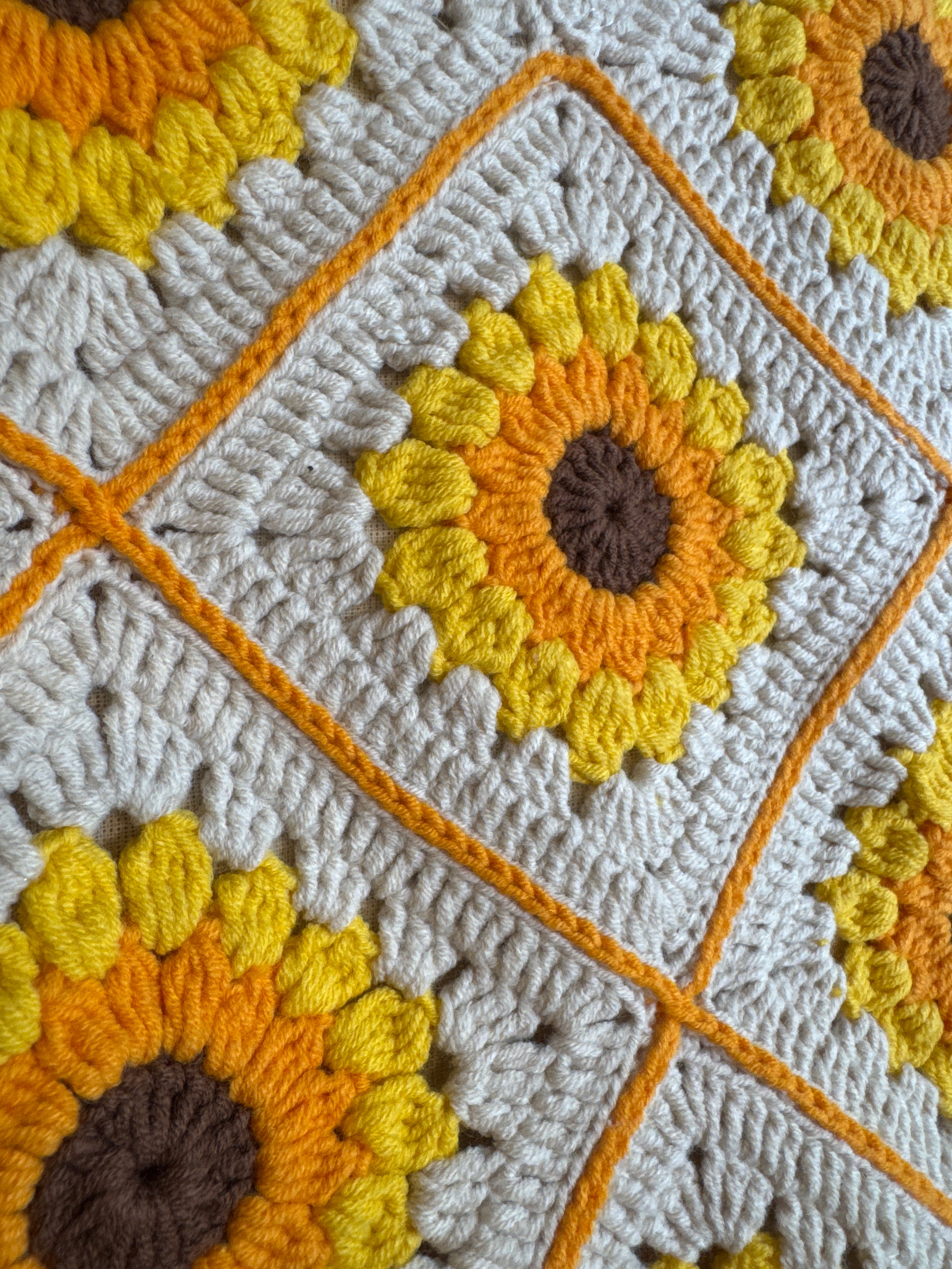 Close-up of a crocheted sunflower square with yellow puff-stitch petals on the cream shoulder bag — handmade by Ana Chic