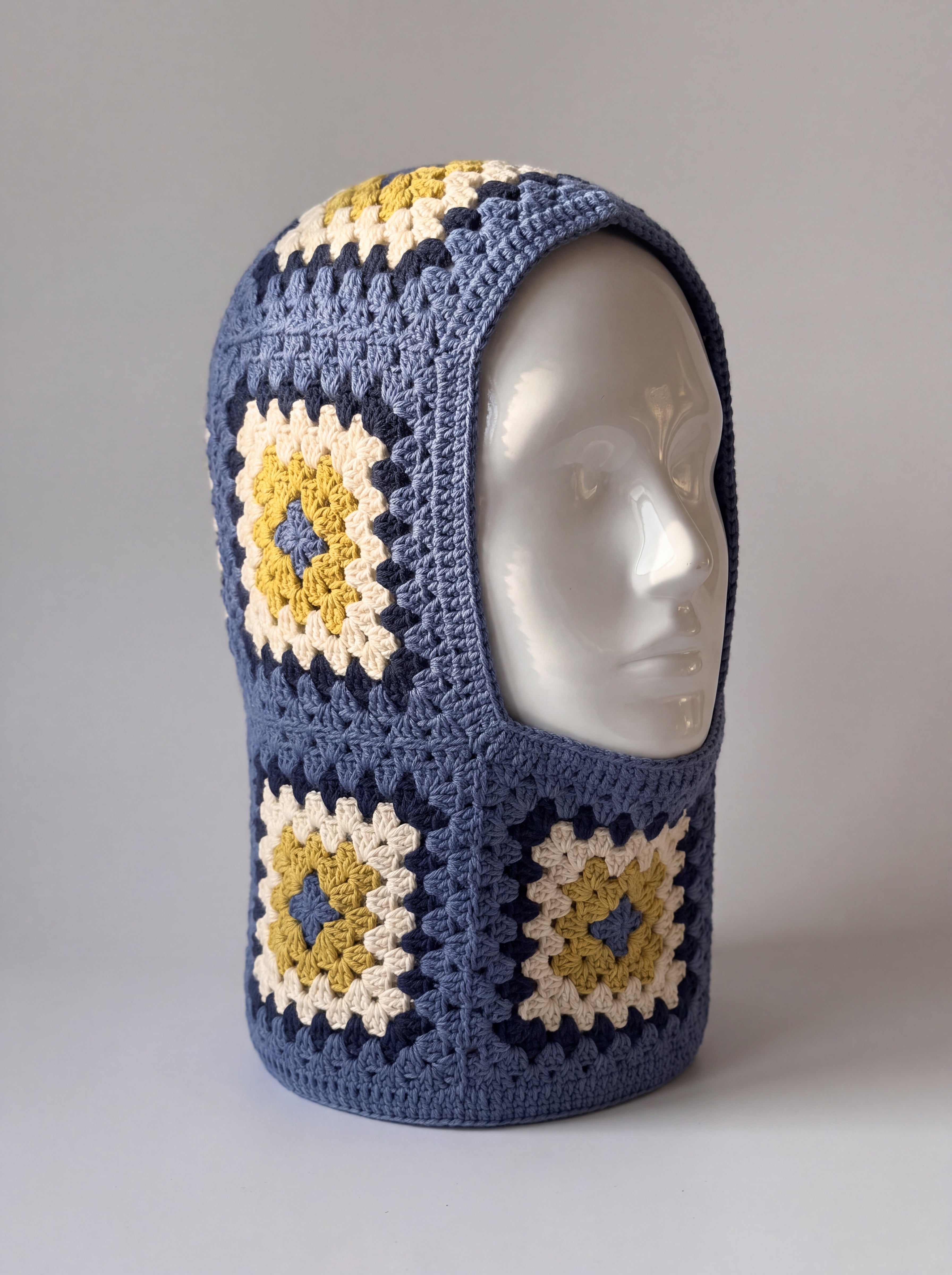 Denim blue and mustard granny square balaclava on a display head, open face and deep neck section — handmade by Ana Chic