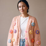 Woman wearing the Daisy Peach cardigan — peach chunky hand-knitted wool cardigan with pastel puff-stitch flowers over a white T-shirt, handmade by Ana Chic