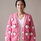 Woman wearing the Rose Bubblegum cardigan — bubblegum pink chunky hand-knitted wool cardigan with crocheted white roses over a white V-neck, handmade by Ana Chic