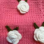 Close-up of crocheted white roses with green leaves on pink chunky knit — handmade by Ana Chic