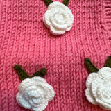 Close-up of crocheted white roses with green leaves on pink chunky knit — handmade by Ana Chic