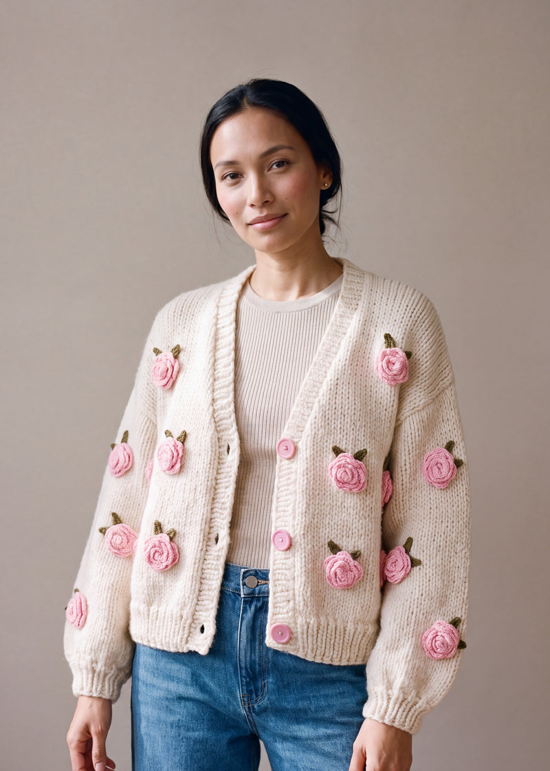 Woman wearing the Rose Cream cardigan — cream chunky hand-knitted wool cardigan with crocheted pink roses over a beige ribbed top, handmade by Ana Chic