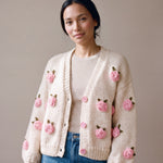 Woman wearing the Rose Cream cardigan — cream chunky hand-knitted wool cardigan with crocheted pink roses over a beige ribbed top, handmade by Ana Chic