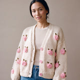 Woman wearing the Rose Cream cardigan — cream chunky hand-knitted wool cardigan with crocheted pink roses over a beige ribbed top, handmade by Ana Chic
