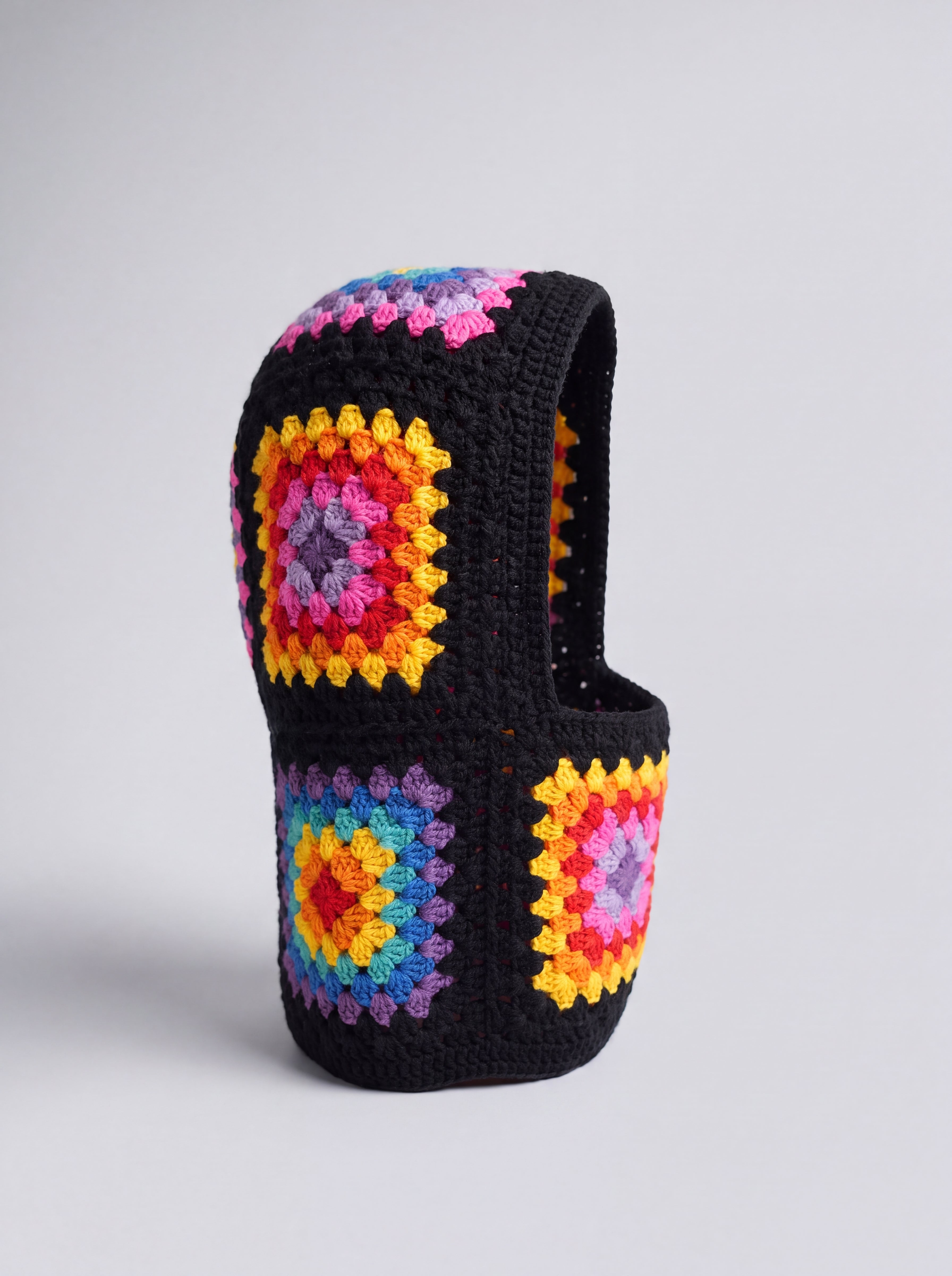Black rainbow granny square balaclava standing on its own, back view of the hood — handmade by Ana Chic