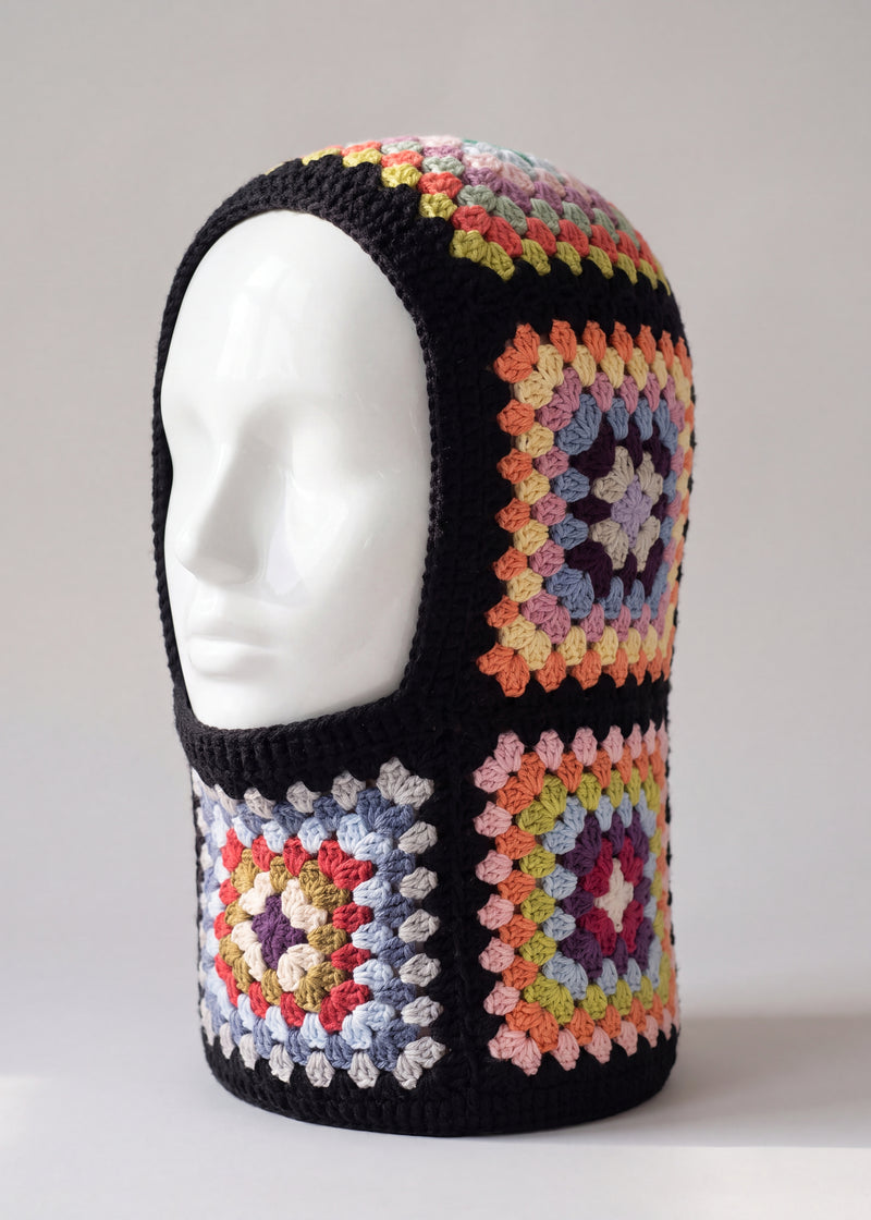 Black pastel granny square balaclava on a display head, open face and deep neck section — handmade by Ana Chic