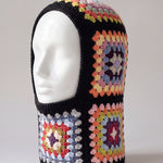 Black pastel granny square balaclava on a display head, open face and deep neck section — handmade by Ana Chic