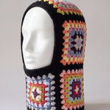 Black pastel granny square balaclava on a display head, open face and deep neck section — handmade by Ana Chic