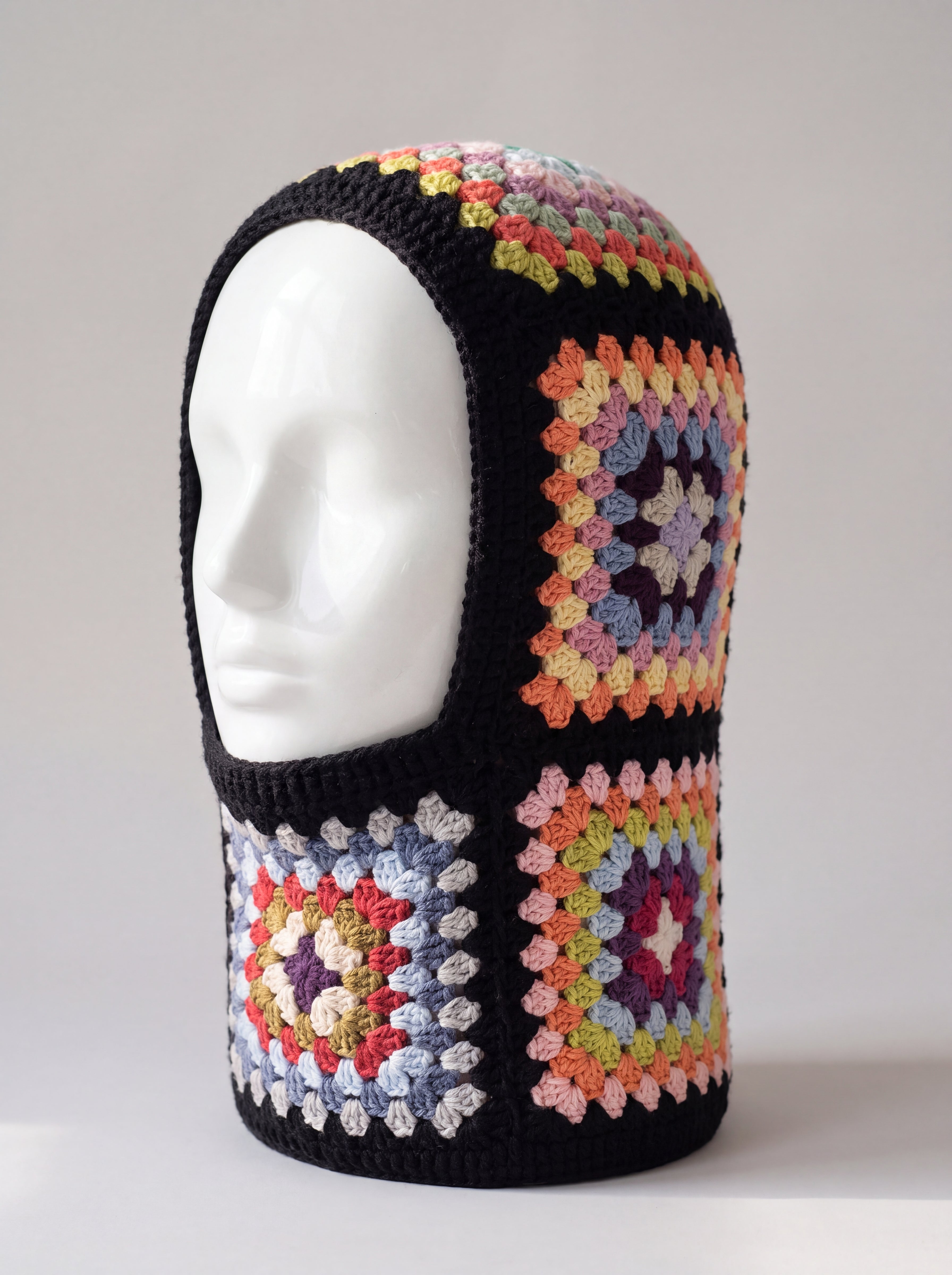 Black pastel granny square balaclava on a display head, open face and deep neck section — handmade by Ana Chic