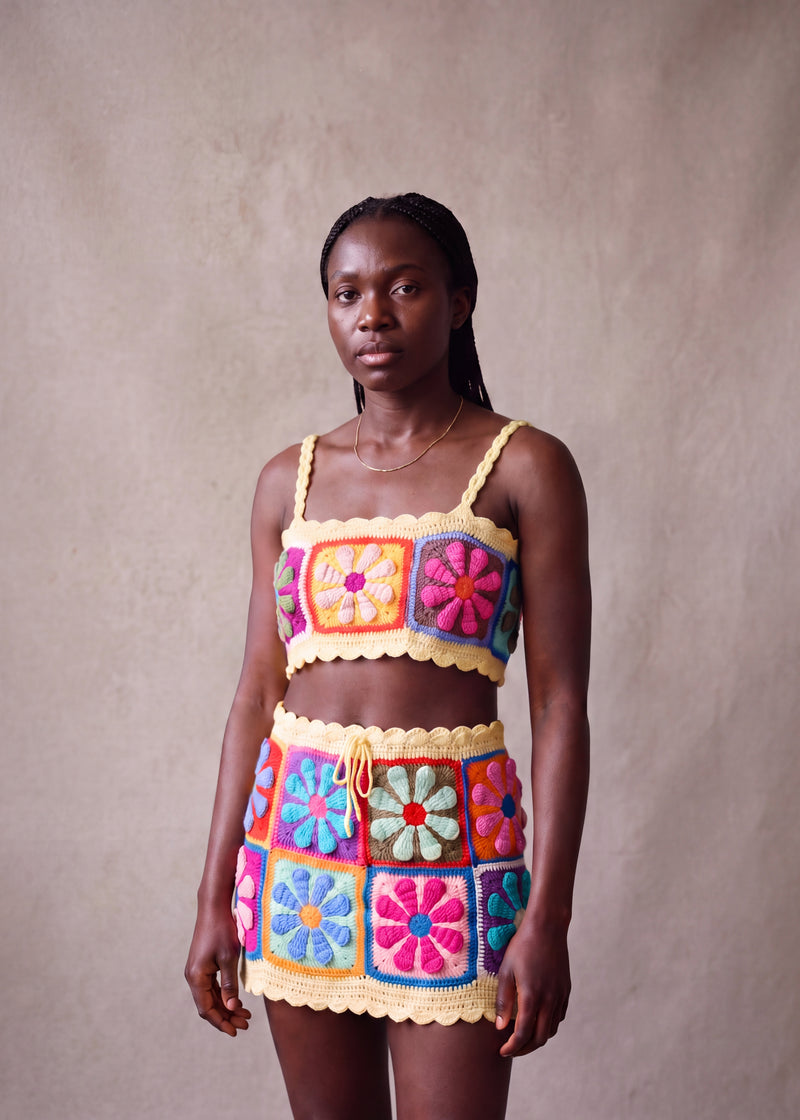 Model wearing the Sunny Petal Set, front view — daisy granny-square crop top and mini skirt in multicolour crochet with butter-yellow scalloped trim, handmade by Ana Chic