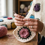 Hands crocheting a dusty-pink layered rose on a cream granny square with an olive leaf round — handmade by Ana Chic