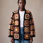 Black Boho Cardi worn by a model, open granny-square crochet cardigan in rust, mustard and cream over a white tee