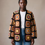 Black Boho Cardi worn by a model, open granny-square crochet cardigan in rust, mustard and cream over a white tee