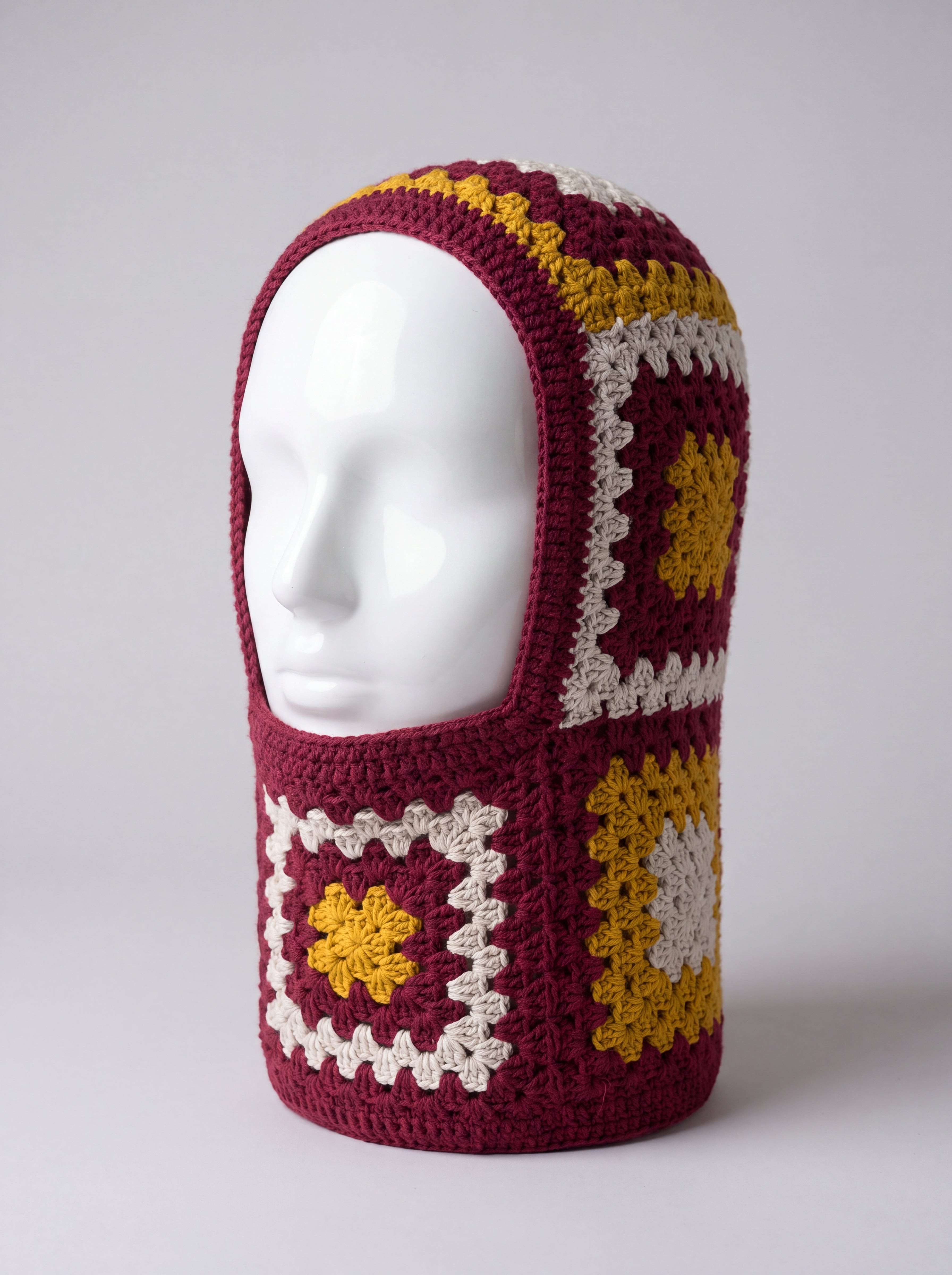 Burgundy and mustard granny square balaclava on a display head, open face and deep neck section — handmade by Ana Chic