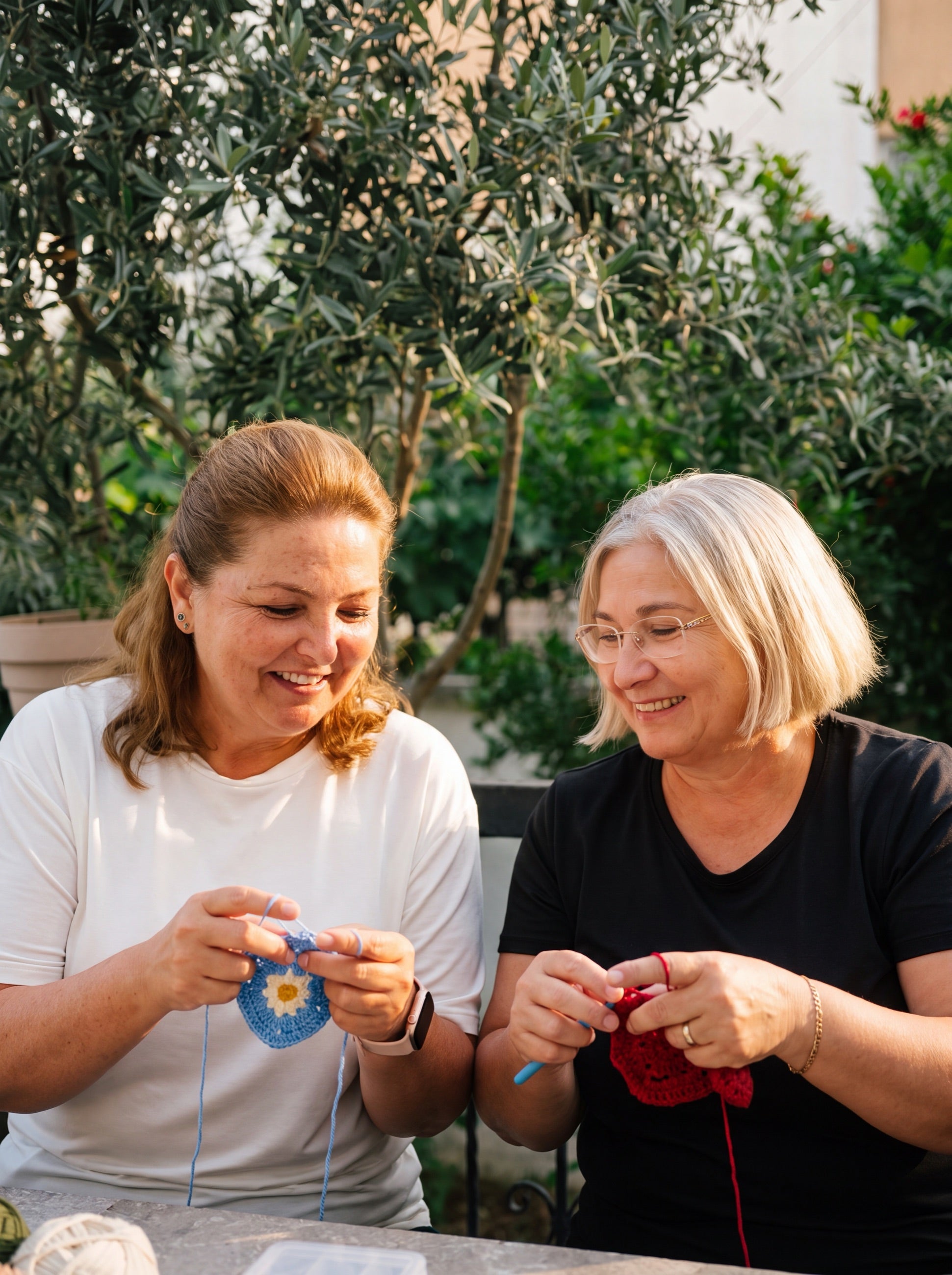 Two makers laughing over crochet work at a garden table