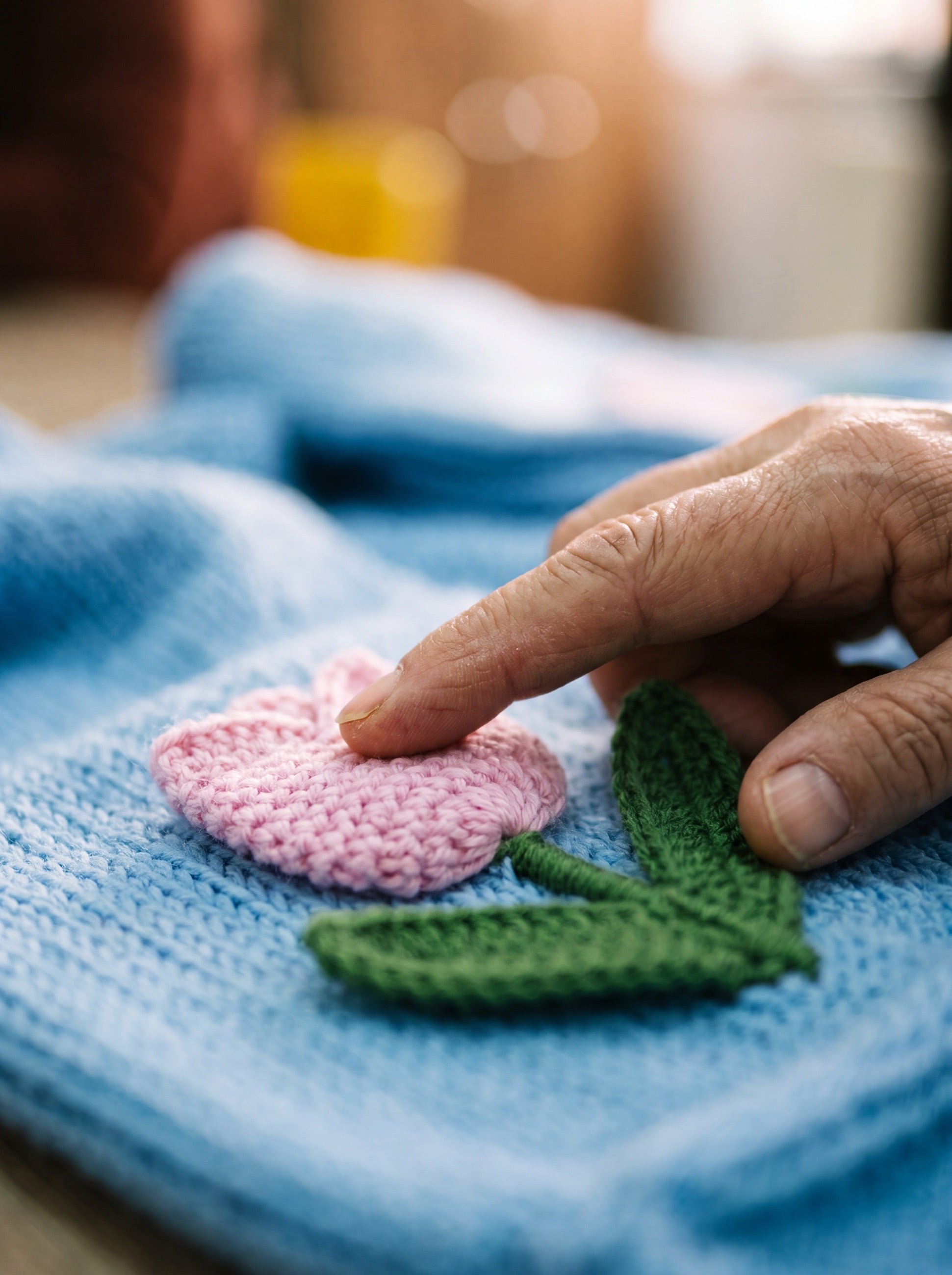 A fingertip resting on a pink crochet tulip stitched to a blue hand-knitted cardigan