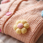 Detail of the Daisy Peach cardigan — a crocheted butter-yellow puff-stitch flower and pink buttons on peach chunky hand-knitted wool, handmade by Ana Chic