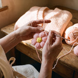 Hands crocheting a pastel pink puff-stitch flower for the Daisy Peach cardigan in the atelier — handmade by Ana Chic