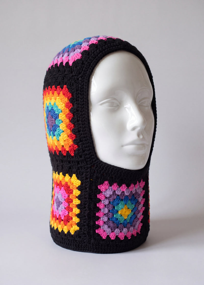 Black rainbow granny square balaclava on a display head, open face and deep neck section — handmade by Ana Chic