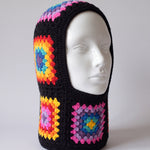 Black rainbow granny square balaclava on a display head, open face and deep neck section — handmade by Ana Chic