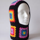 Black rainbow granny square balaclava on a display head, open face and deep neck section — handmade by Ana Chic