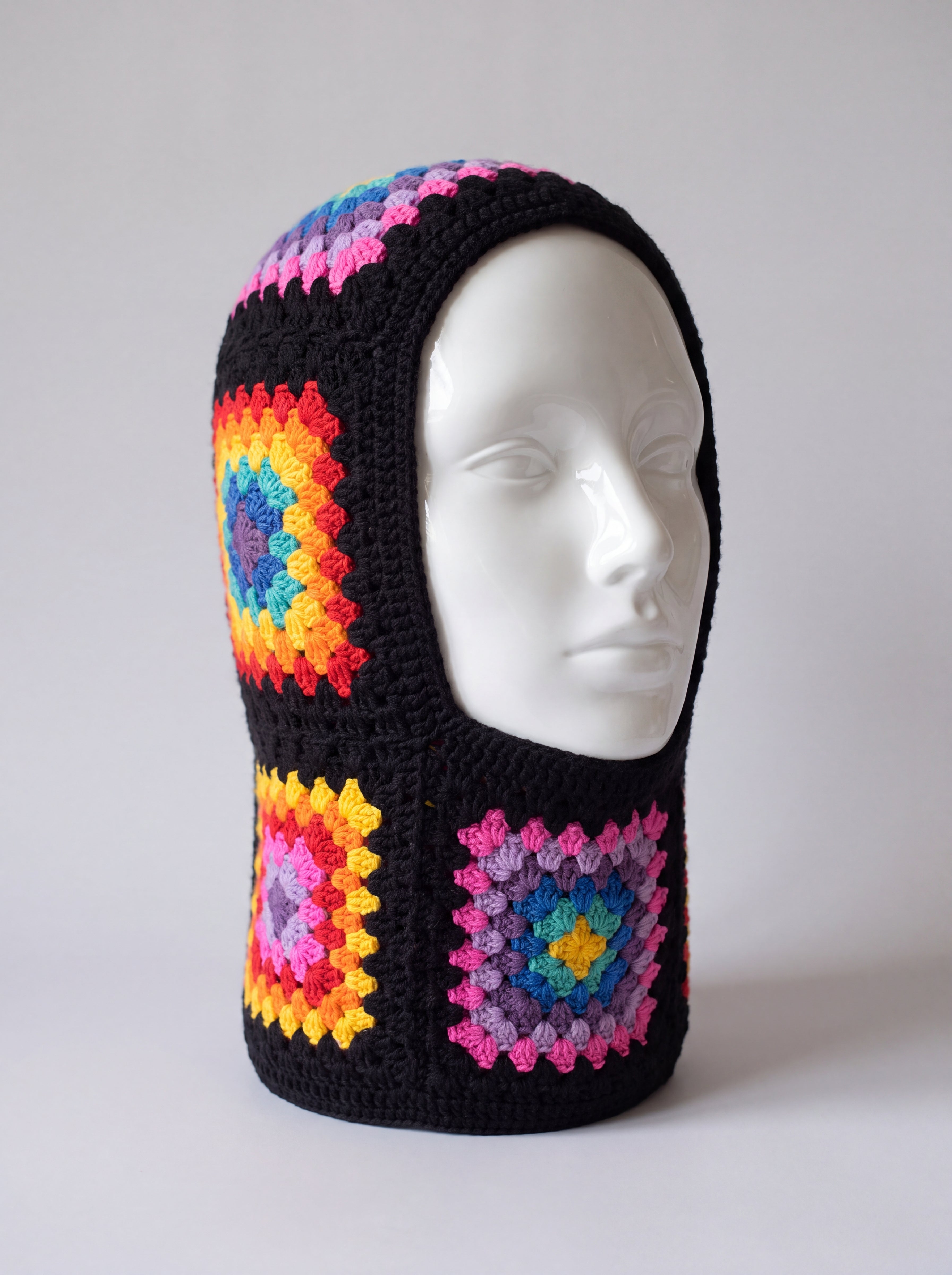 Black rainbow granny square balaclava on a display head, open face and deep neck section — handmade by Ana Chic