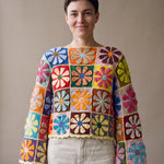 Woman wearing the Flower Jumper, a handmade crochet granny-square jumper with flat daisy motifs, boat neckline and wide bell sleeves, styled with ecru jeans