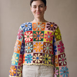 Woman wearing the Flower Jumper, a handmade crochet granny-square jumper with flat daisy motifs, boat neckline and wide bell sleeves, styled with ecru jeans