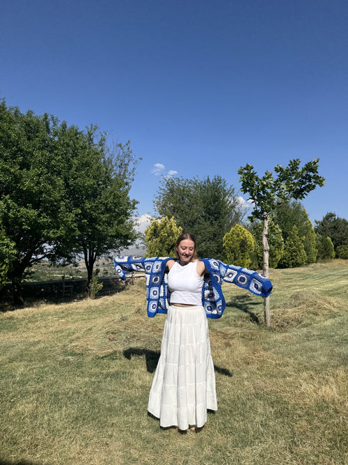 Customer in a white dress holding a blue crochet shawl outdoors
