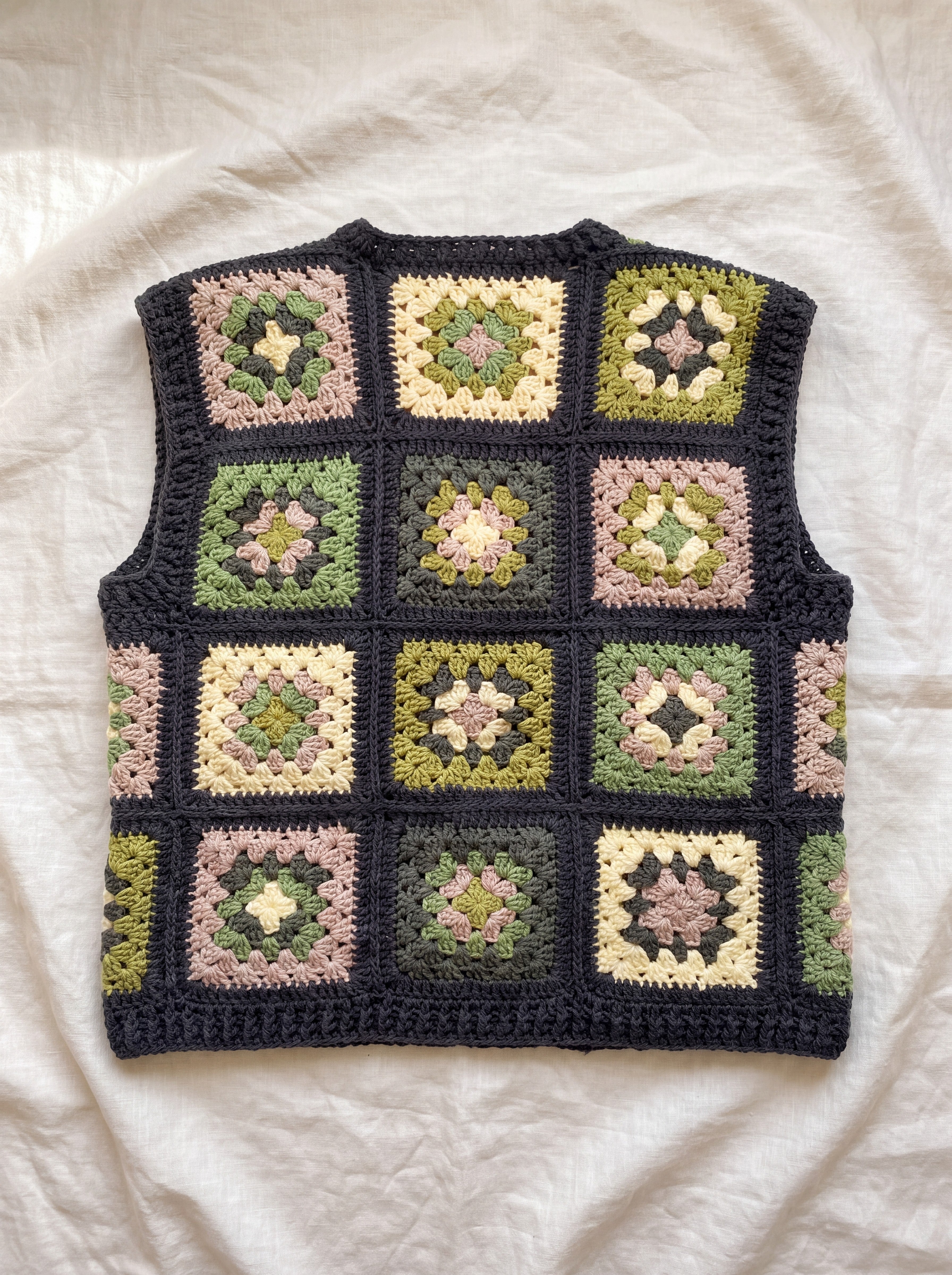 Green granny square crochet vest, back, laid flat on linen