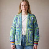 Woman wearing a lime, aqua and denim-blue granny square cardigan with rainbow cuffs — handmade by Ana Chic