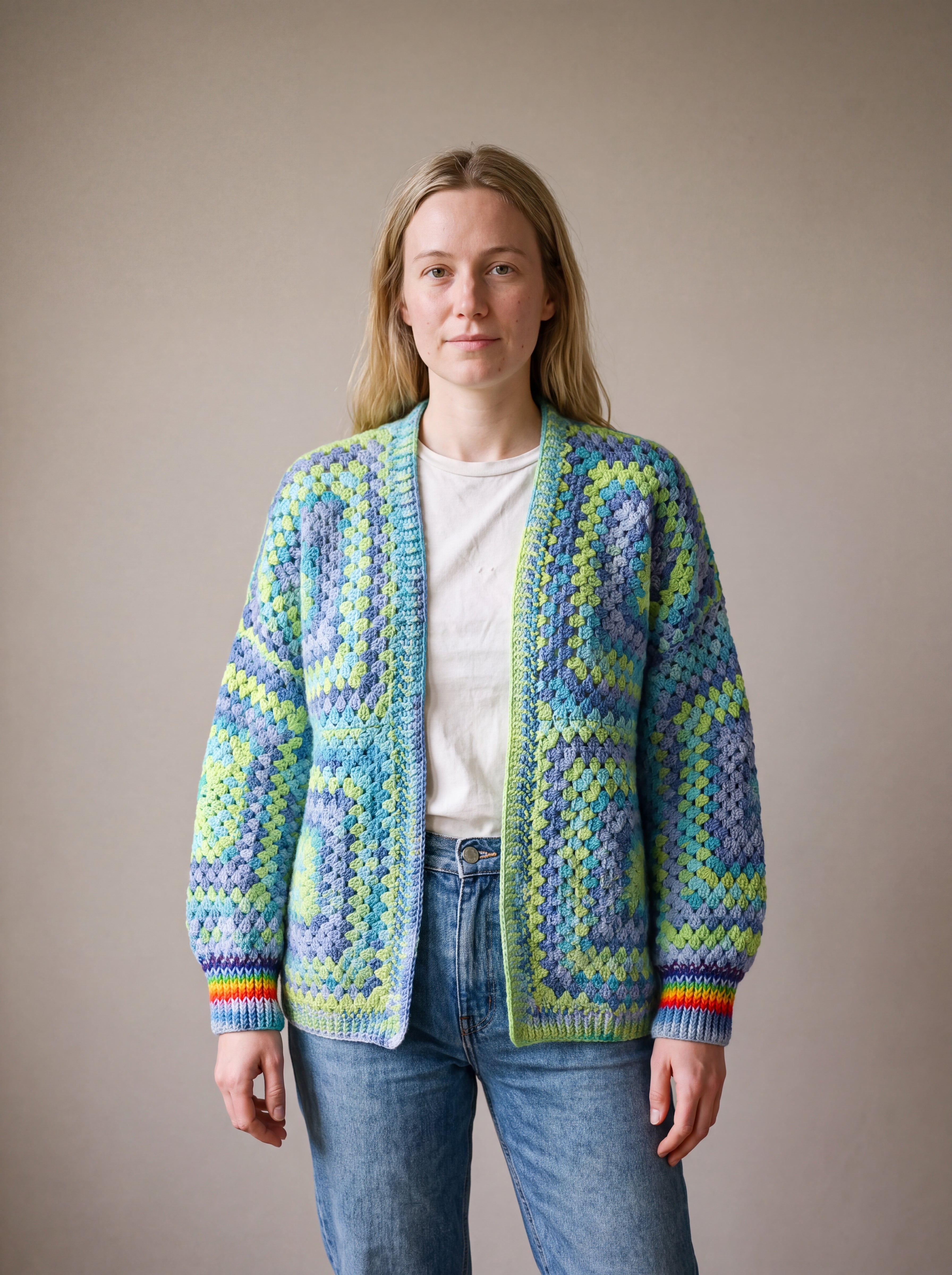 Woman wearing a lime, aqua and denim-blue granny square cardigan with rainbow cuffs — handmade by Ana Chic