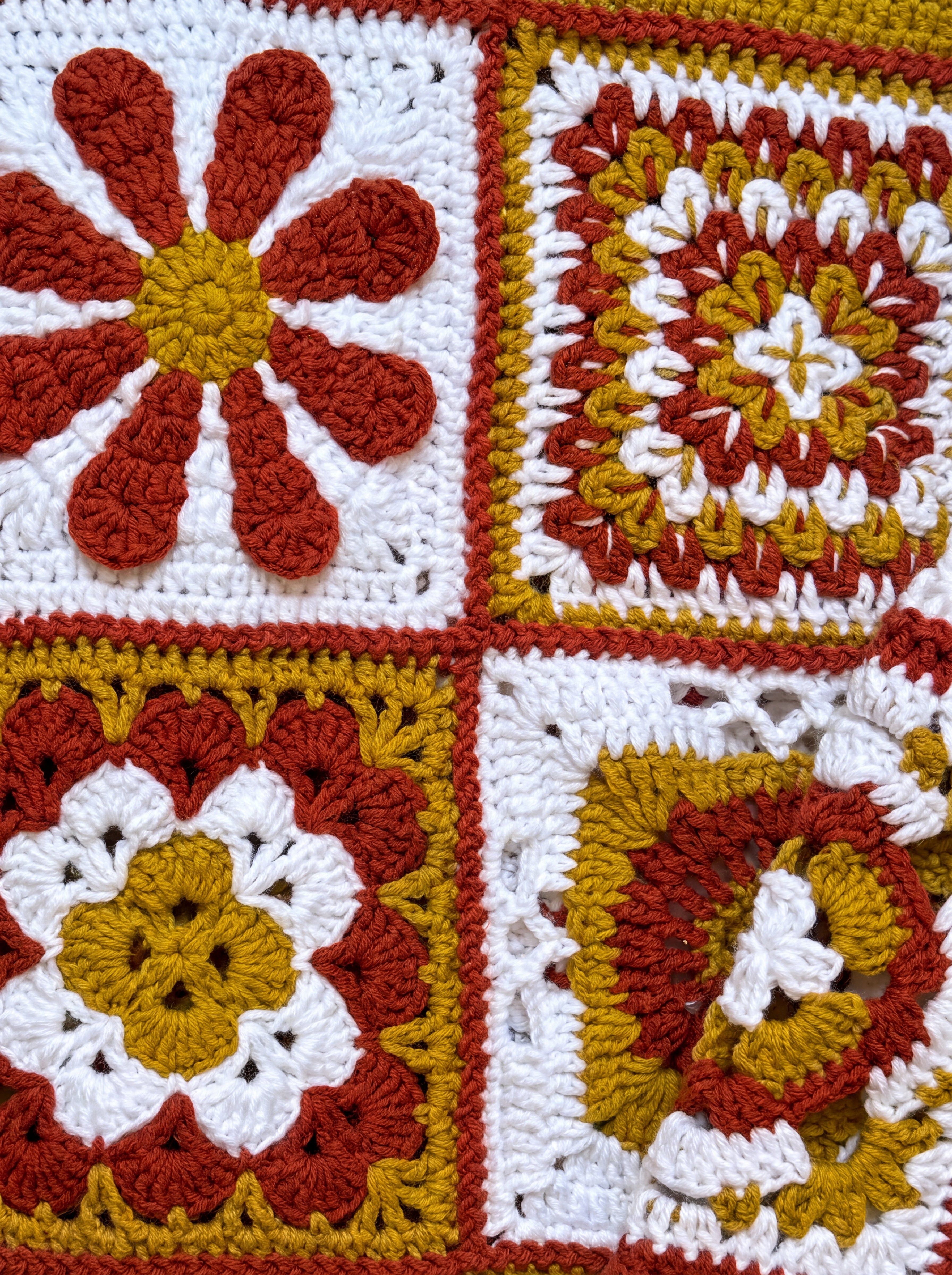 Close-up of four different hand-crocheted squares on the Sampler Cardigan in Rust, each a different motif design