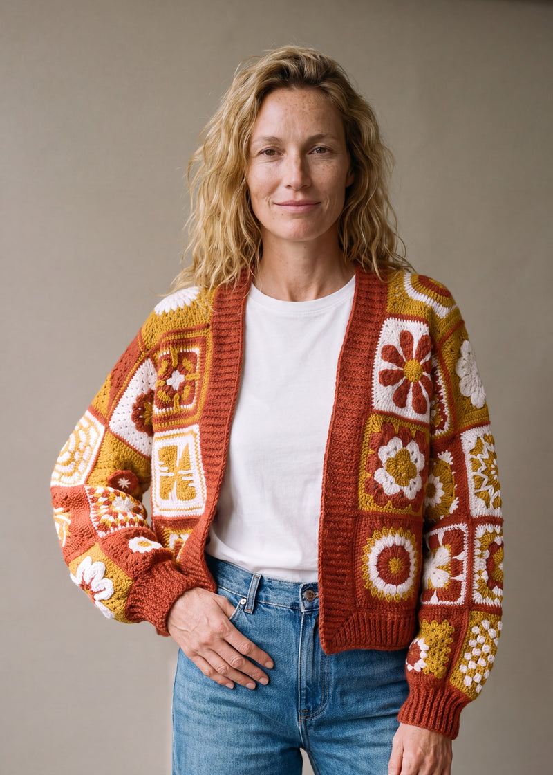 Woman wearing the Sampler Cardigan in Rust, a hand-crocheted granny-square cardigan, over a plain t-shirt and jeans