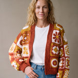 Woman wearing the Sampler Cardigan in Rust, a hand-crocheted granny-square cardigan, over a plain t-shirt and jeans