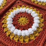 Macro of a hand-crocheted square with a ring of popcorn bobbles on the Sampler Cardigan in Rust