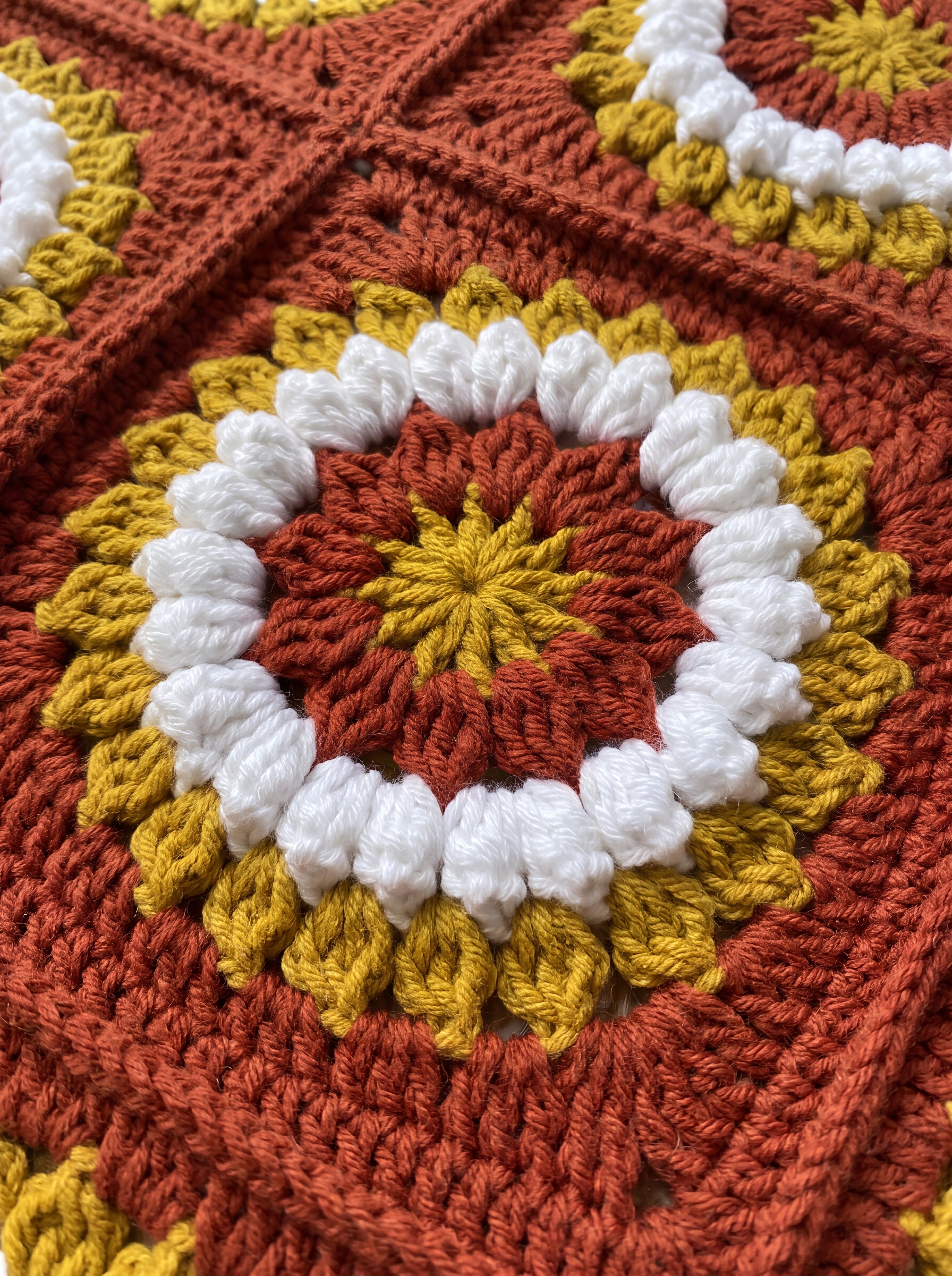 Macro of a hand-crocheted square with a ring of popcorn bobbles on the Sampler Cardigan in Rust