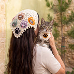 Woman wearing the large cat-face crochet bandana over her hair, holding a tabby cat in the matching small paw bandana — handmade by Ana Chic