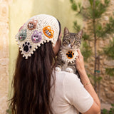 Woman wearing the large cat-face crochet bandana over her hair, holding a tabby cat in the matching small paw bandana — handmade by Ana Chic