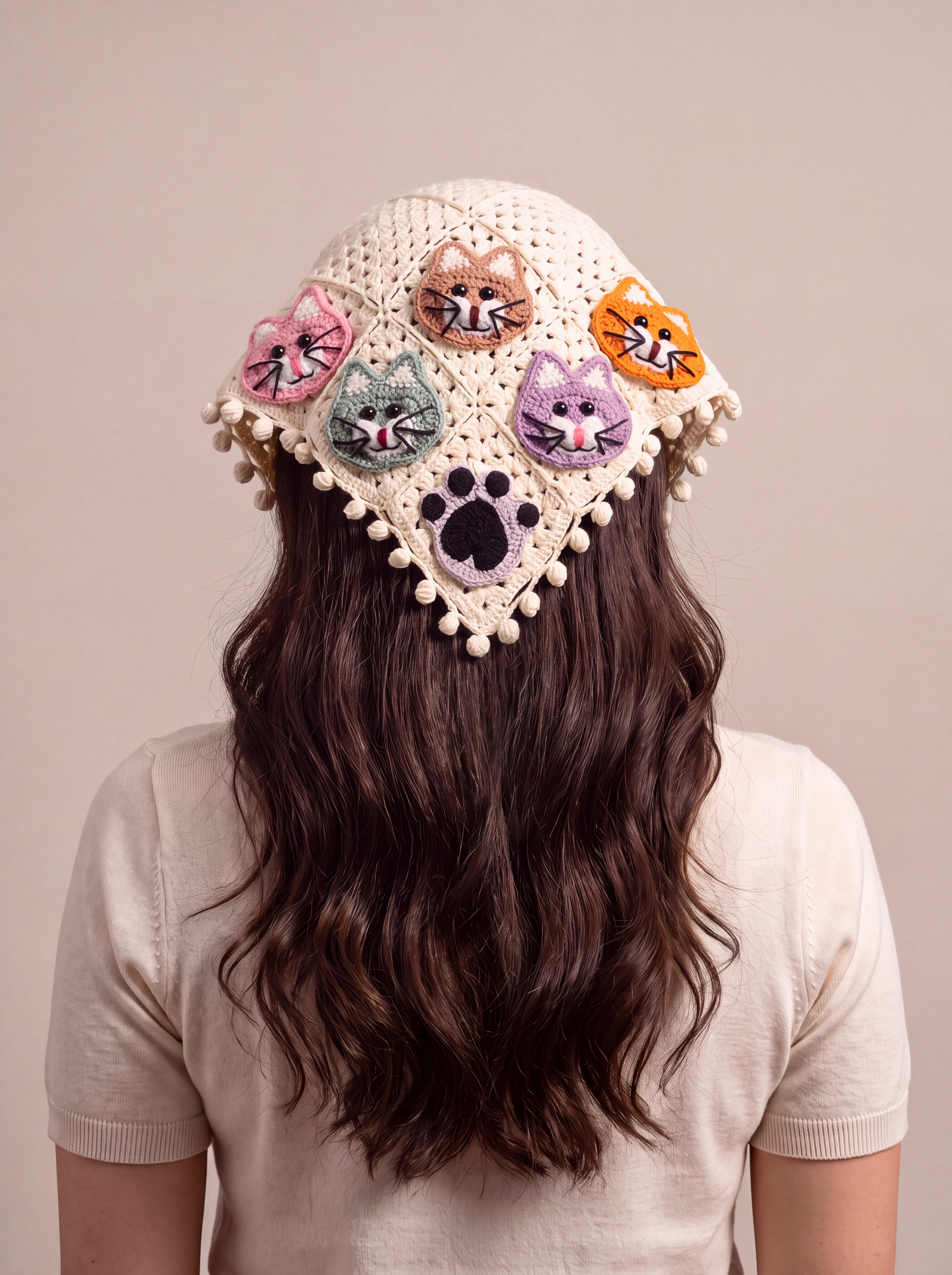 Back view of the large crochet bandana worn over long dark hair, five cat faces and a black paw on cream granny squares — handmade by Ana Chic