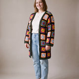 Full-length view of the long black granny square crochet cardigan worn open over a cream top and jeans, size L