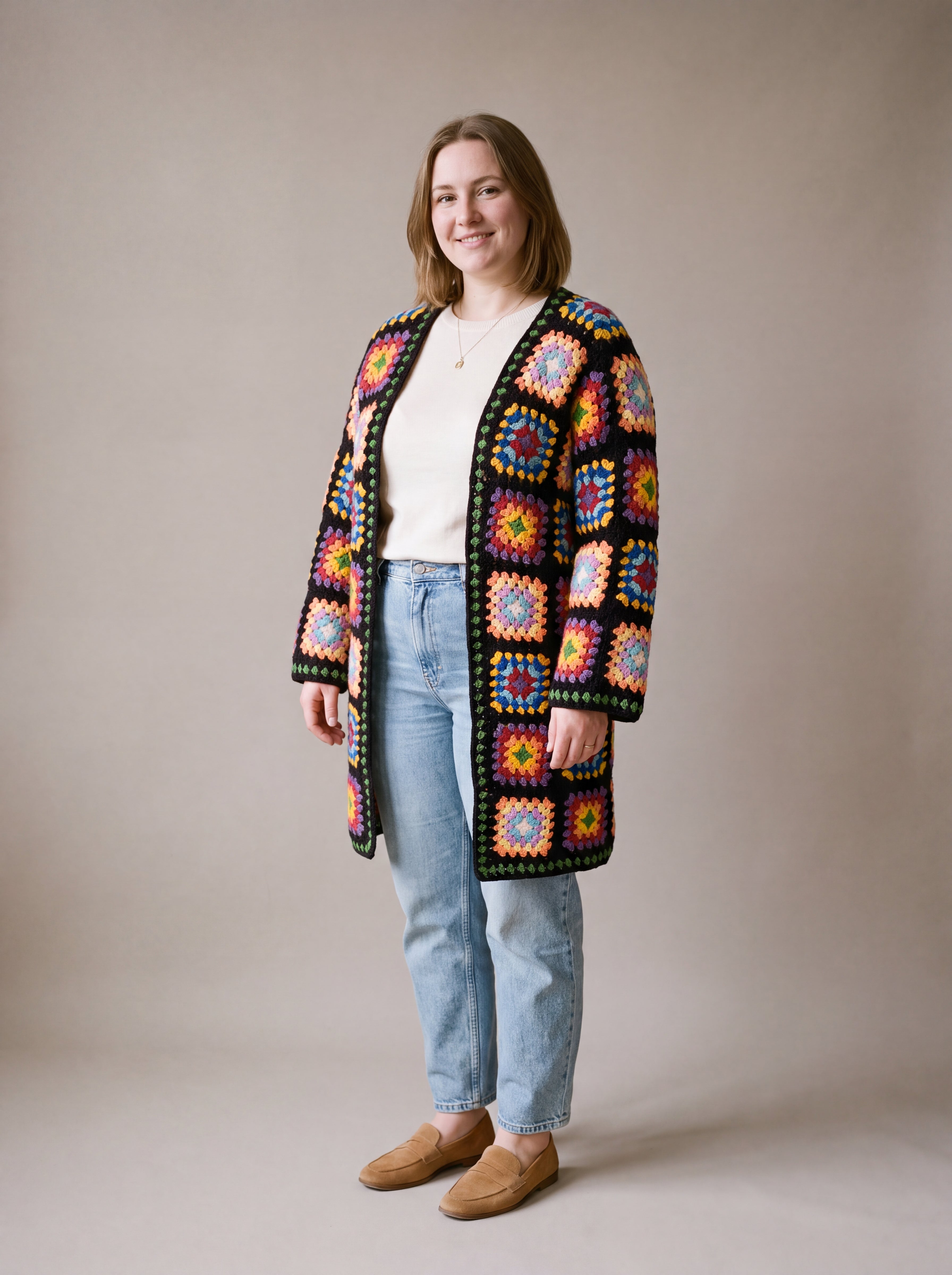 Full-length view of the long black granny square crochet cardigan worn open over a cream top and jeans, size L
