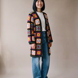 Full-length view of the long black granny square crochet cardigan ending just above the knee, worn with wide-leg jeans, size S