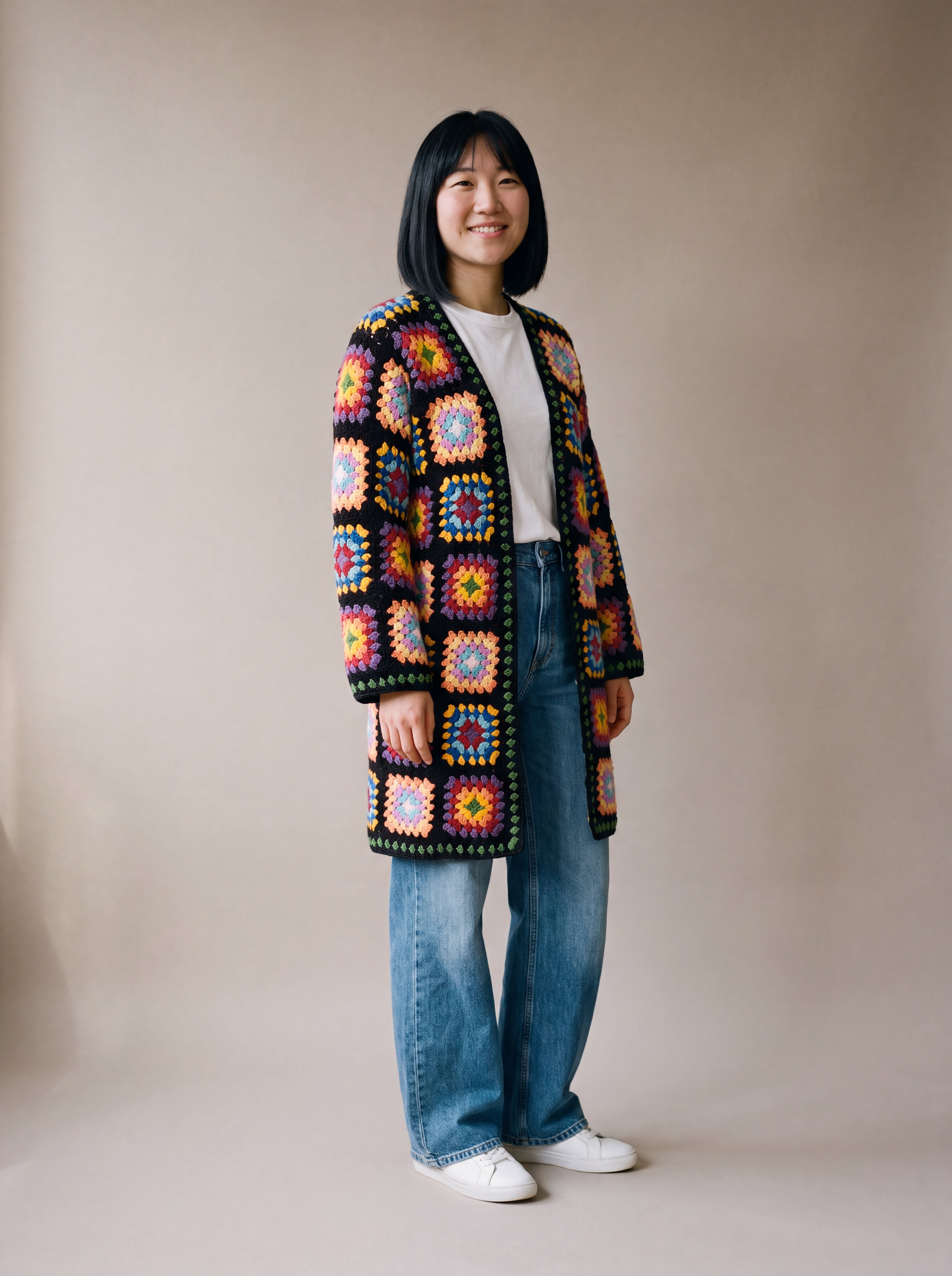 Full-length view of the long black granny square crochet cardigan ending just above the knee, worn with wide-leg jeans, size S
