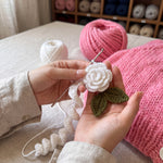 Hands coiling a crocheted white rose for the Rose Bubblegum cardigan in the atelier — handmade by Ana Chic